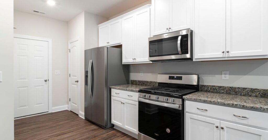 Contemporary kitchen featuring stainless steel fridge and microwave with white cabinetry.